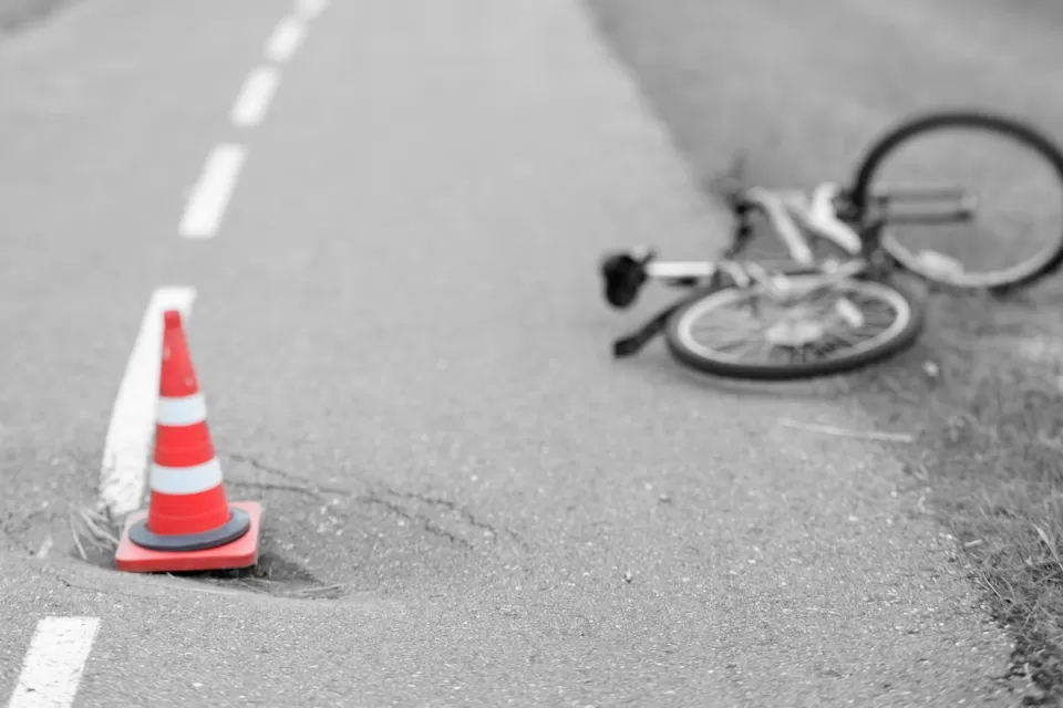 Blurred black and white image of bicycle laying down in road with orange traffic cone in foreground.